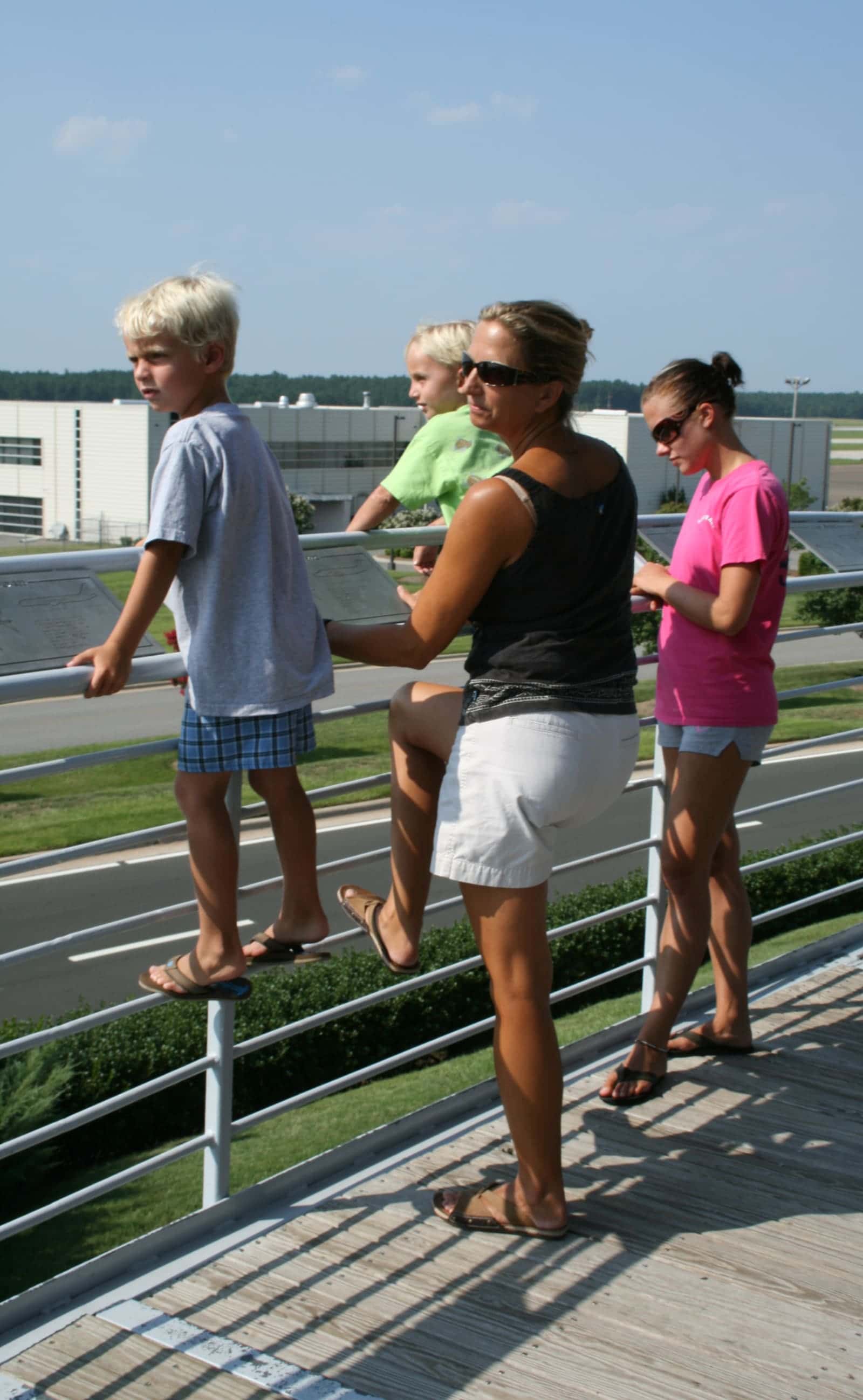 A mother and her children watch planes take off and land at an airport observation area