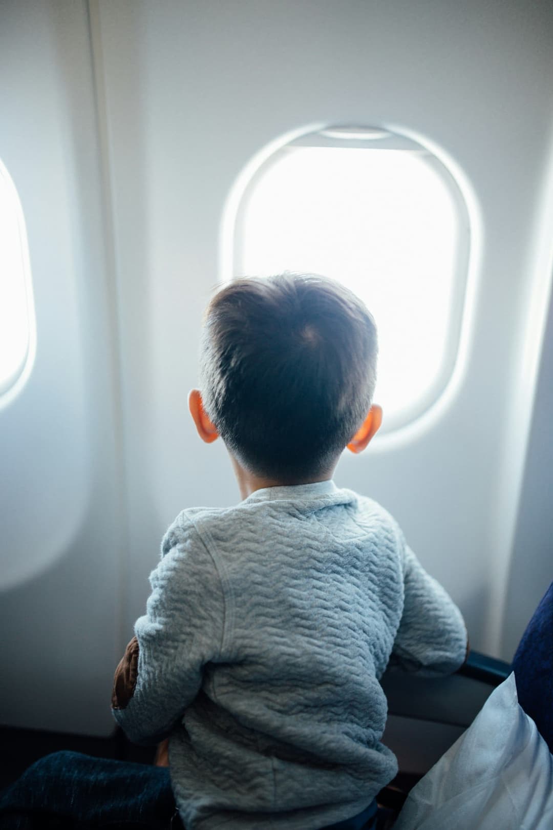 A young boy sits by the airplane window, looking out during flight