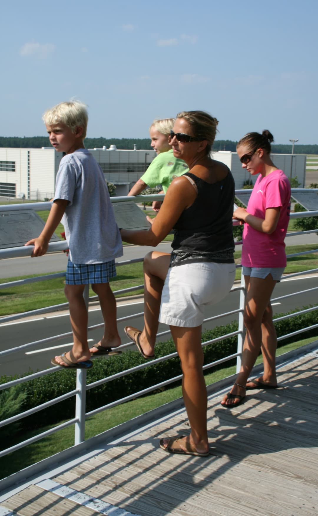 A mother and her children watch planes take off and land at an airport observation area